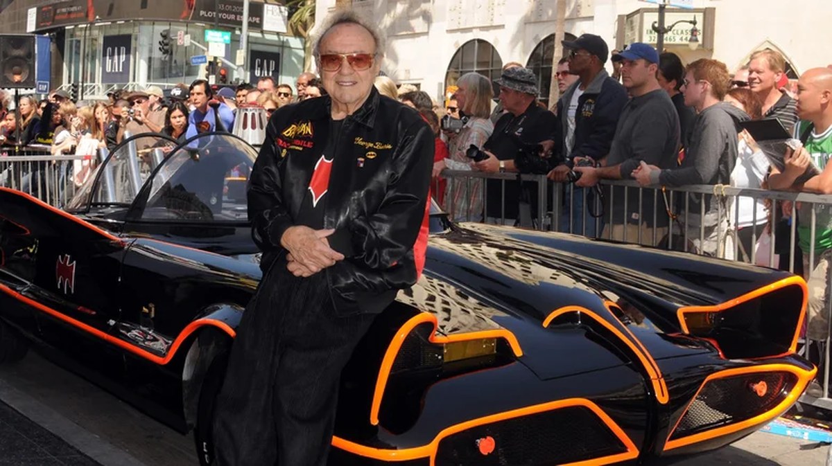 The 1966 Batmobile's front fascia, featuring glossy black paint outlined in bright fluorescent orange pinstriping around the mesh grille, a recessed headlight cavity, and creator George Barris.