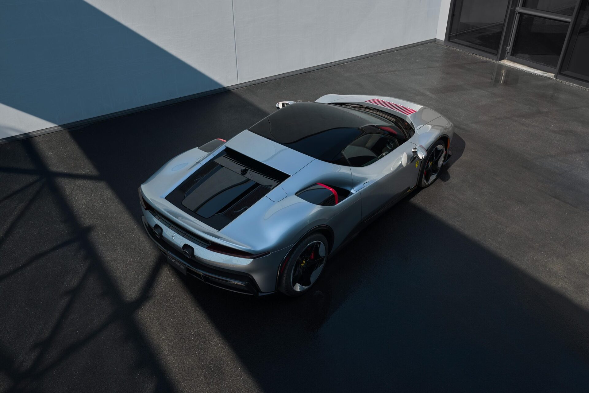 A sleek silver sports car parked on a dark pavement with dramatic shadows.