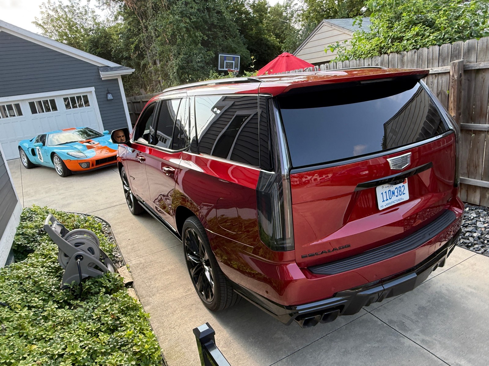 Red Cadillac Escalade parked beside an orange and blue sports car in a residential driveway. Red Cadillac Escalade parked beside an orange and blue sports car in a residential driveway.