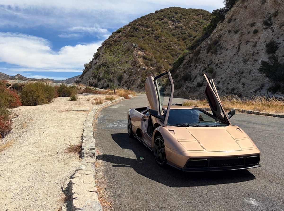 A luxury sports car with butterfly doors parked on a winding road surrounded by hills and greenery under a blue sky. A luxury sports car with butterfly doors parked on a winding road surrounded by hills and greenery under a blue sky.
