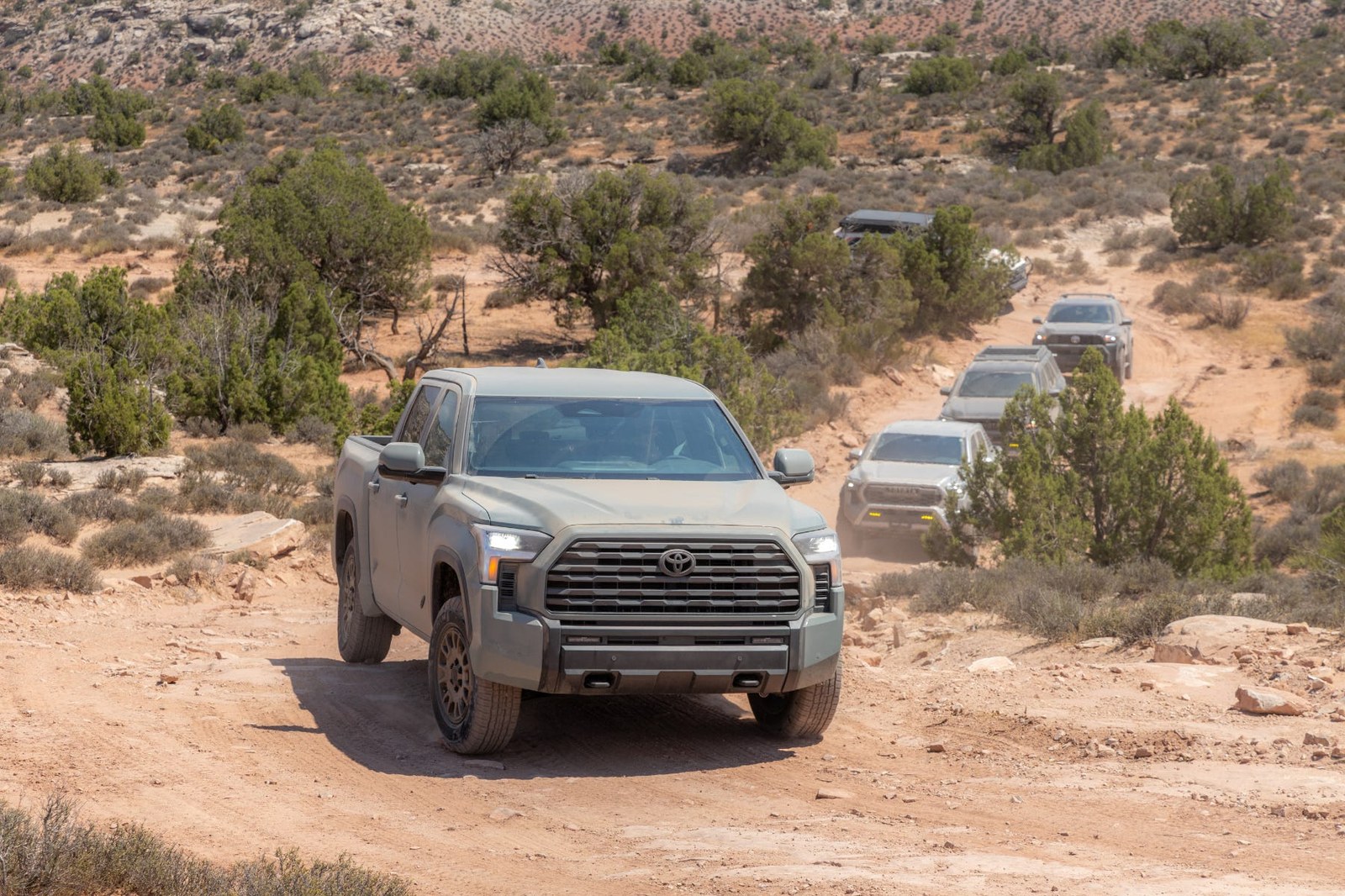 A rugged pickup truck navigating a dirt trail with other vehicles visible in the background. A rugged pickup truck navigating a dirt trail with other vehicles visible in the background.