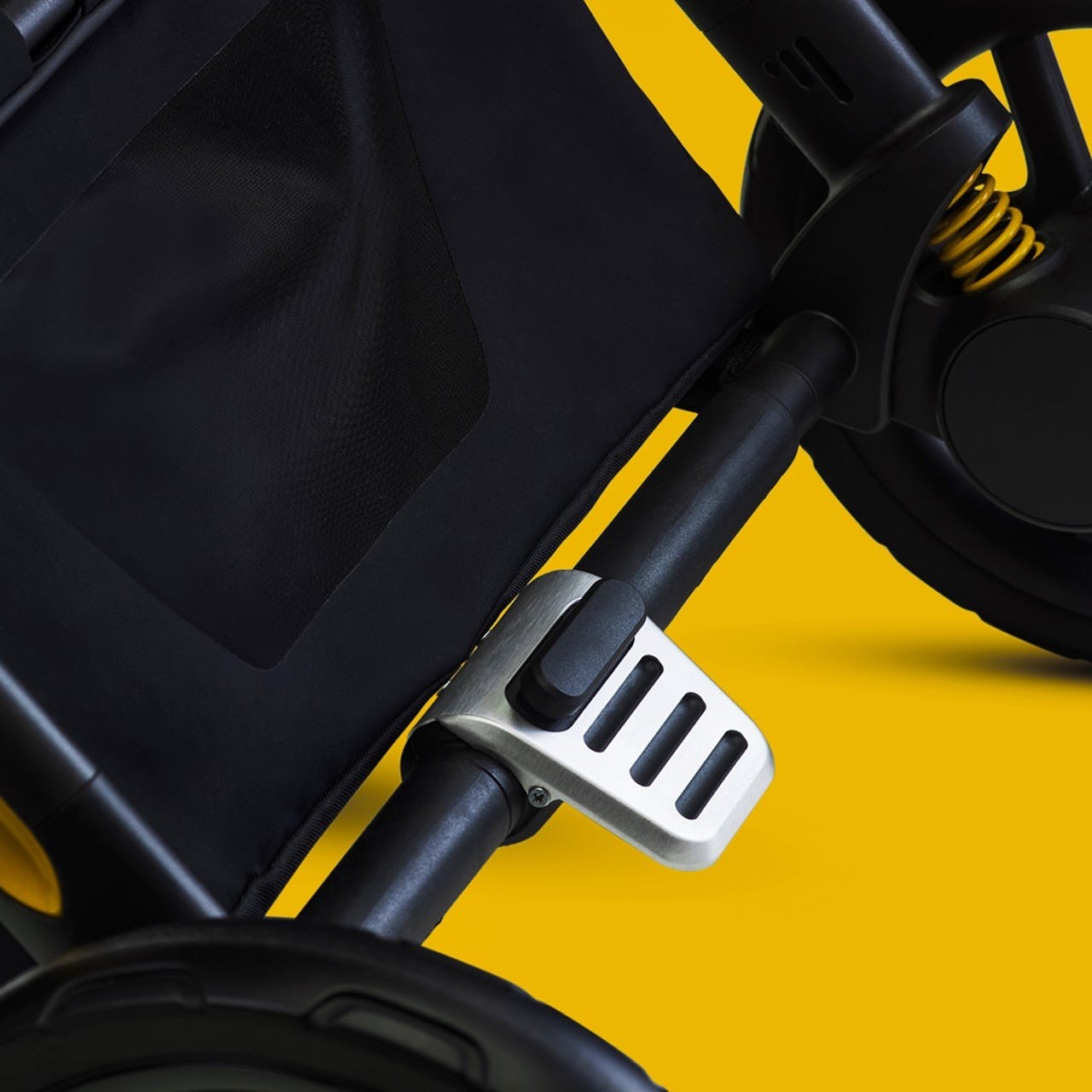 Close-up of a stroller's handle with a metallic locking mechanism against a bright yellow background.