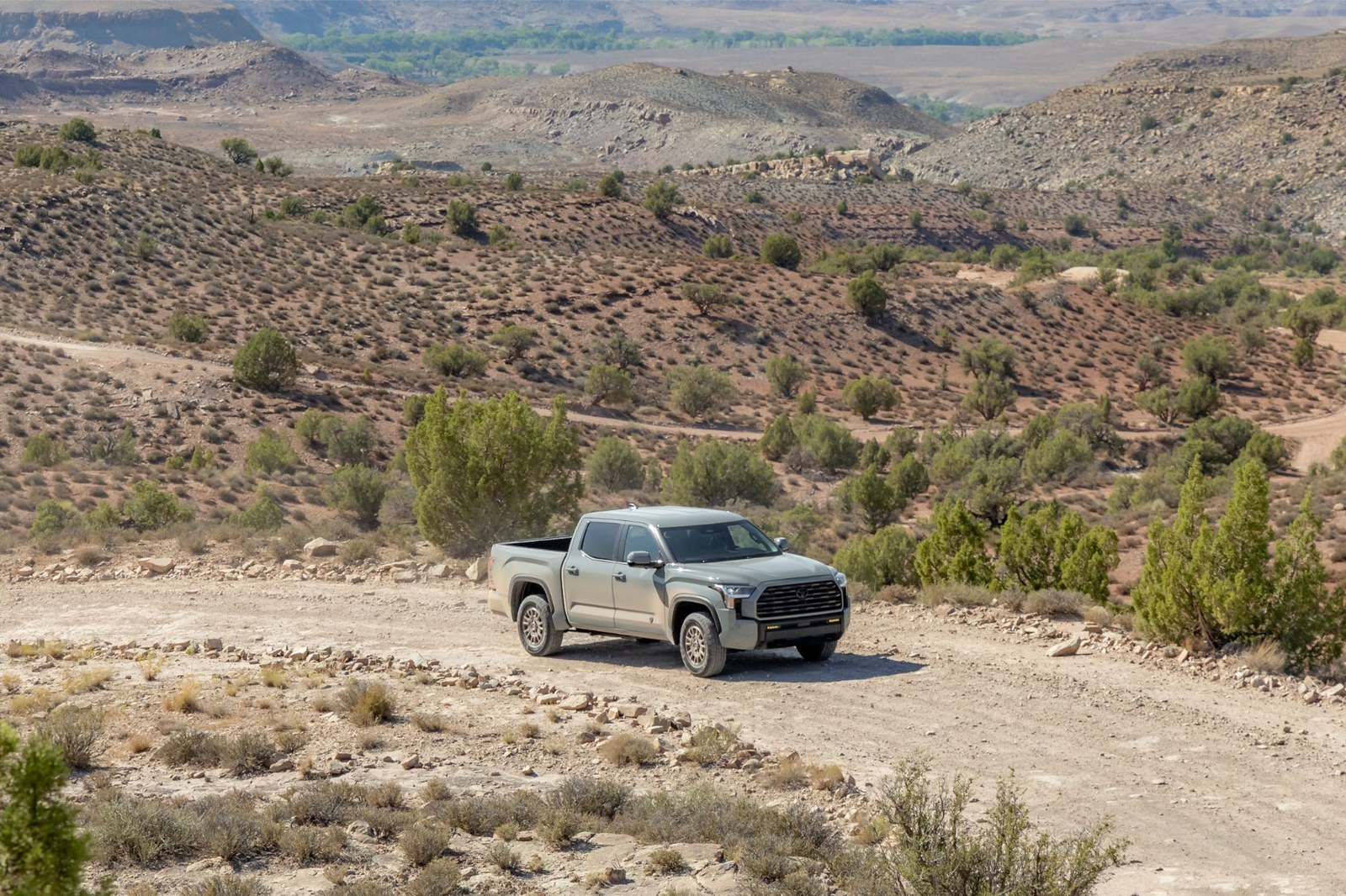 A pickup truck driving along a dirt road in a mountainous, arid landscape with sparse vegetation. A pickup truck driving along a dirt road in a mountainous, arid landscape with sparse vegetation.
