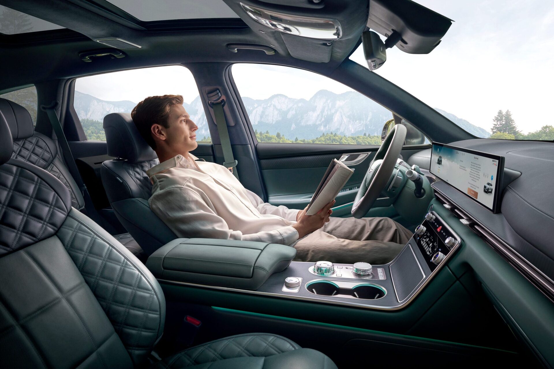 A man reading a book in a modern car interior with scenic mountains visible through the window. A man reading a book in a modern car interior with scenic mountains visible through the window.