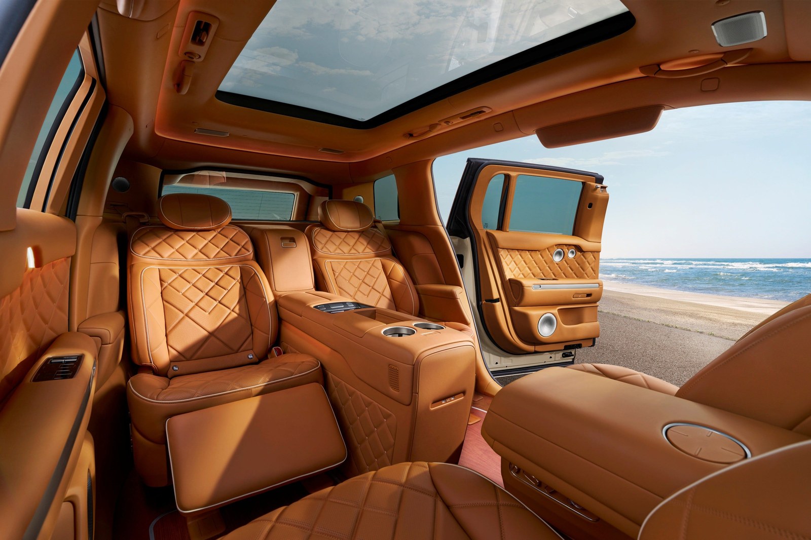 Luxurious car interior with tan leather upholstery, large panoramic sunroof, and ocean view through the open door.