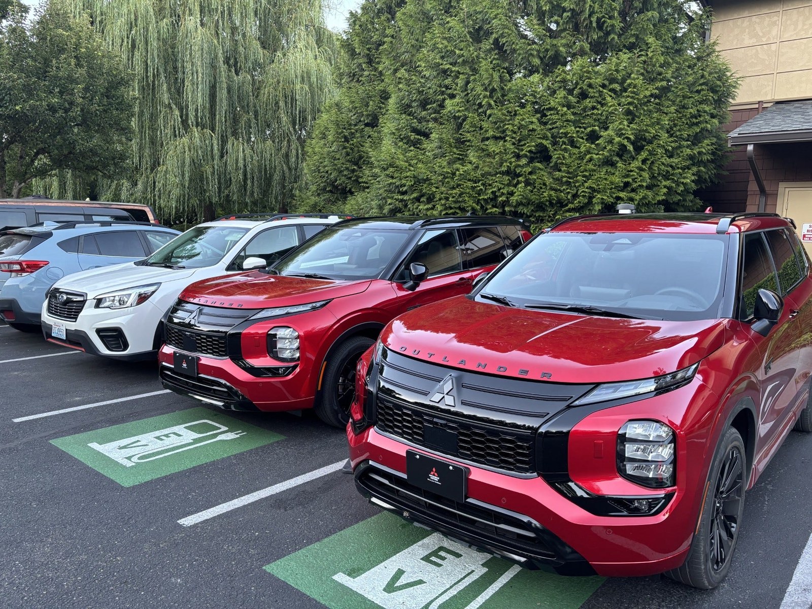 Two red Mitsubishi Outlander SUVs parked next to a white Subaru in an electric vehicle charging area.