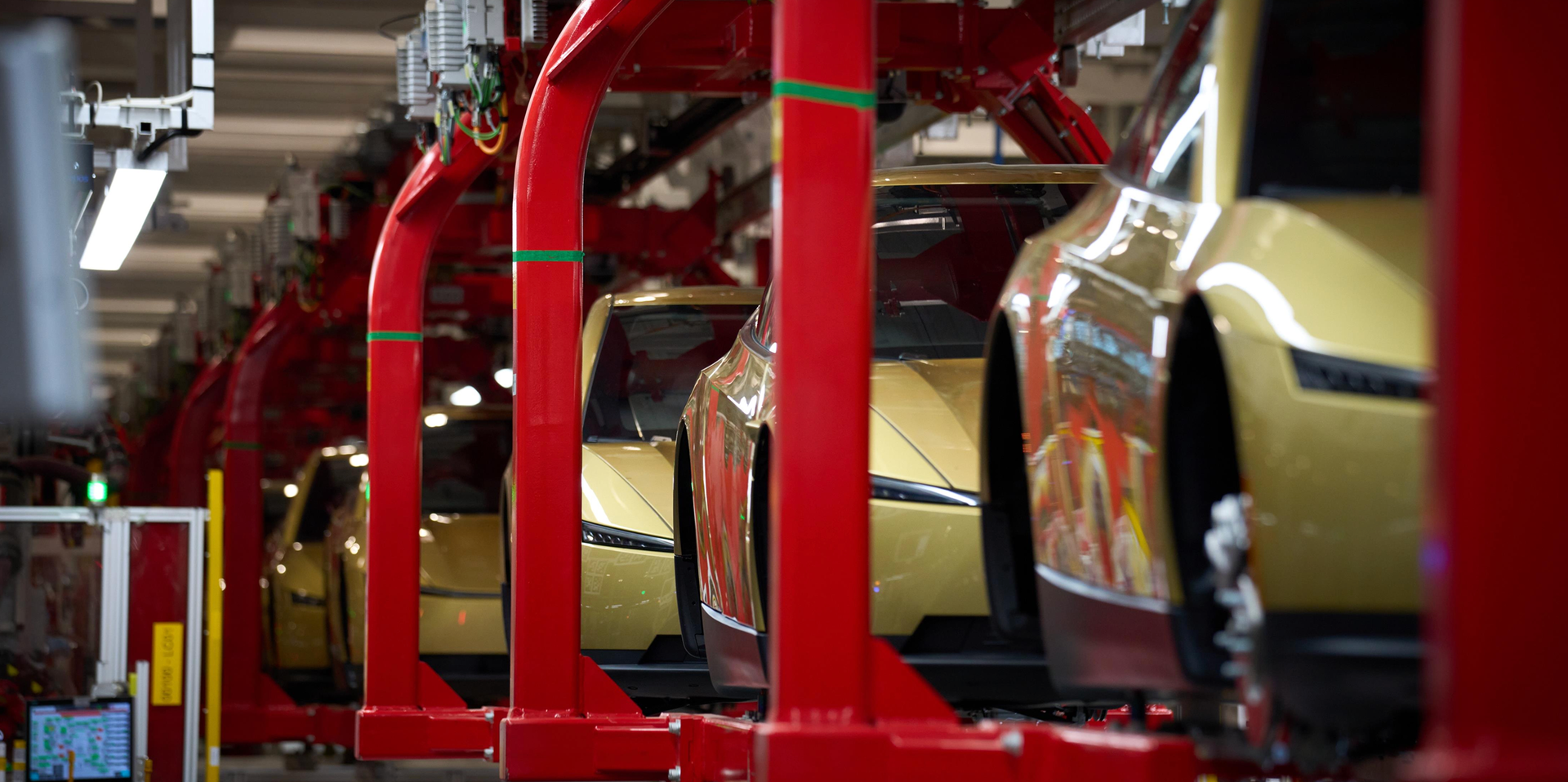 Assembly line featuring yellow cars suspended on a red frame in a manufacturing facility. Assembly line featuring yellow cars suspended on a red frame in a manufacturing facility.