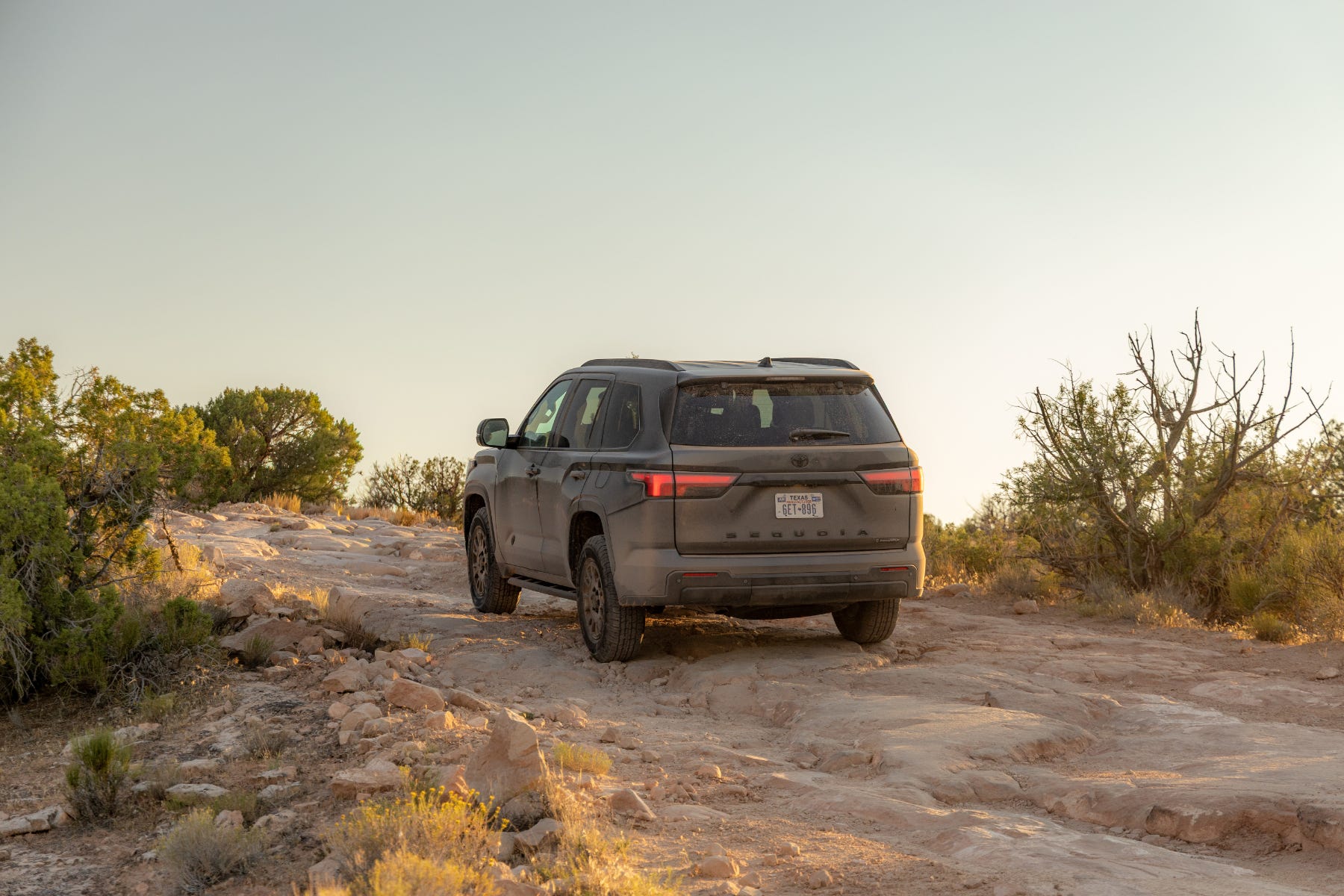 A rugged SUV navigating a rocky terrain under a clear sky, surrounded by sparse vegetation.