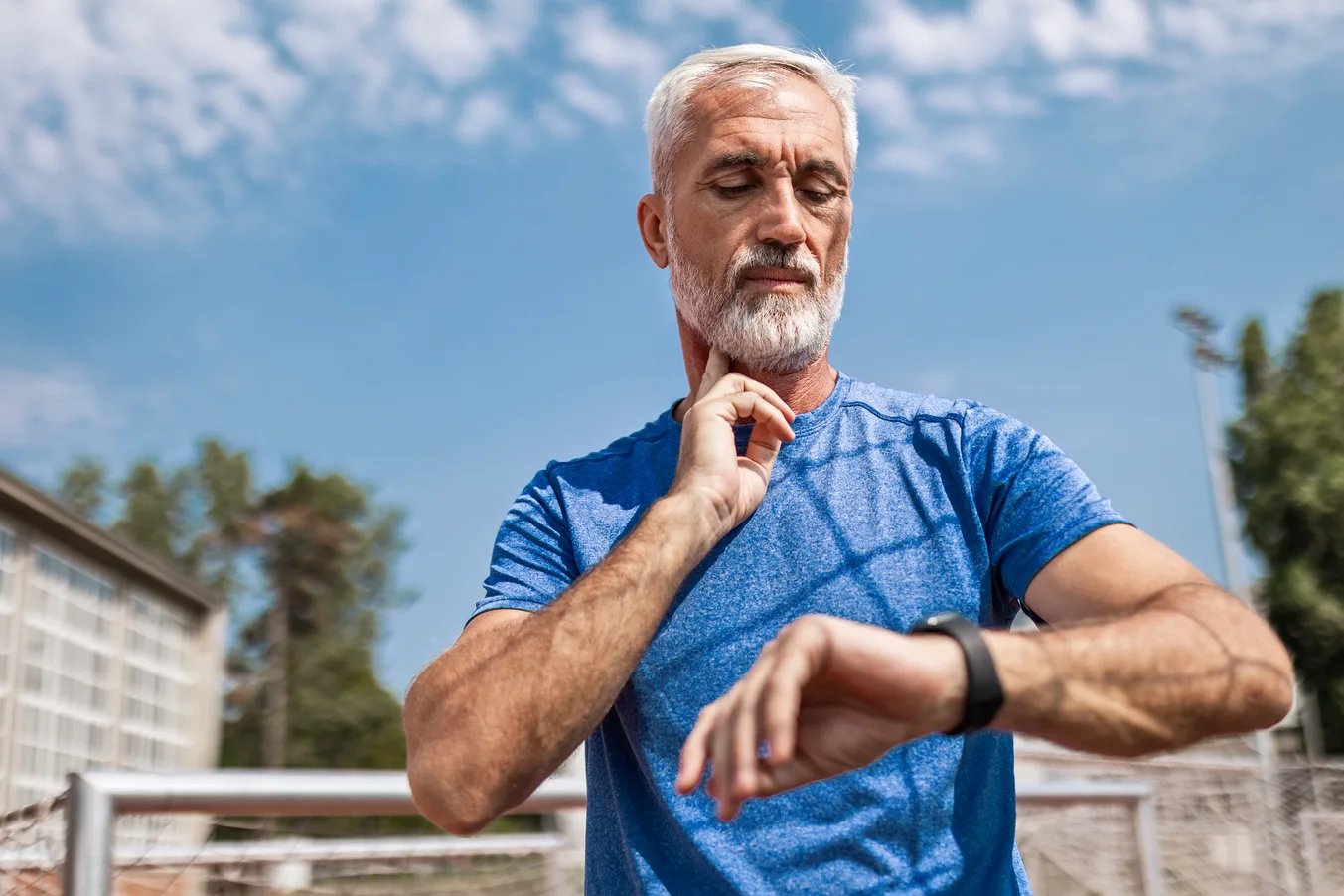 Senior Athlete Taking Pulse at the Stadium Confident senior athlete after running at the sports stadium on a running track taking a break taking pulse