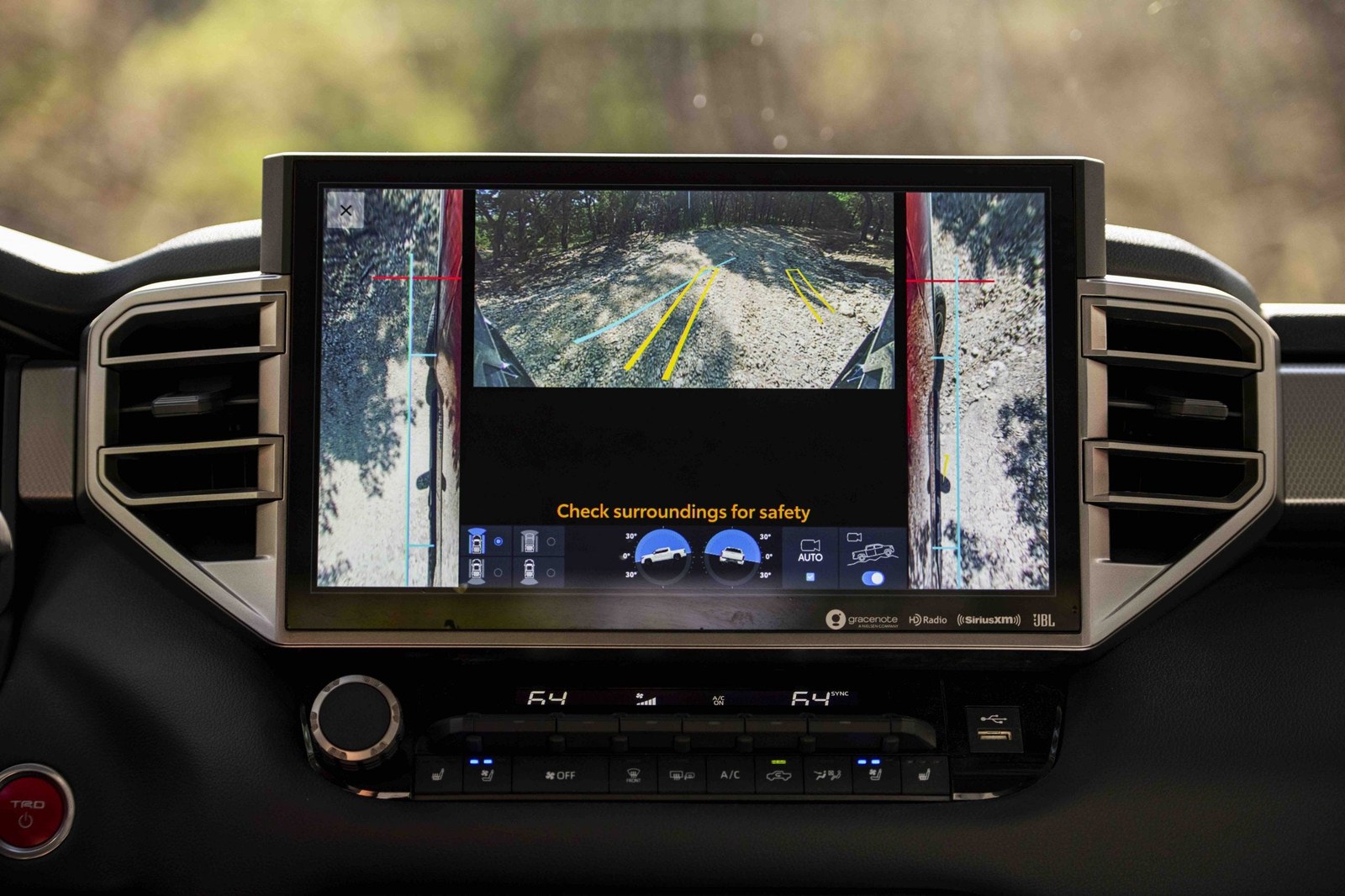 Vehicle dashboard display showing a rearview camera with guidance lines and a safety reminder. Vehicle dashboard display showing a rearview camera with guidance lines and a safety reminder.