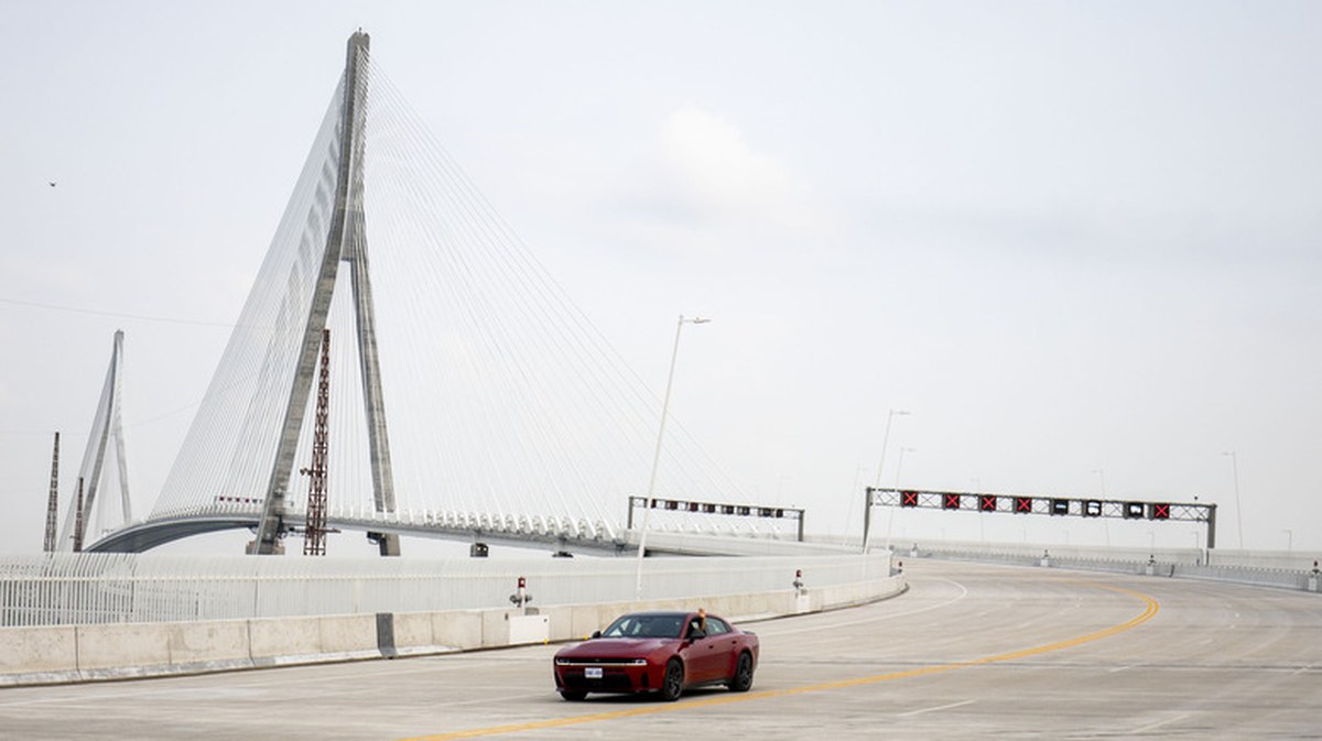 an electric dodge charger drives down an empty Gordie Howe International bridge on a cloudy day