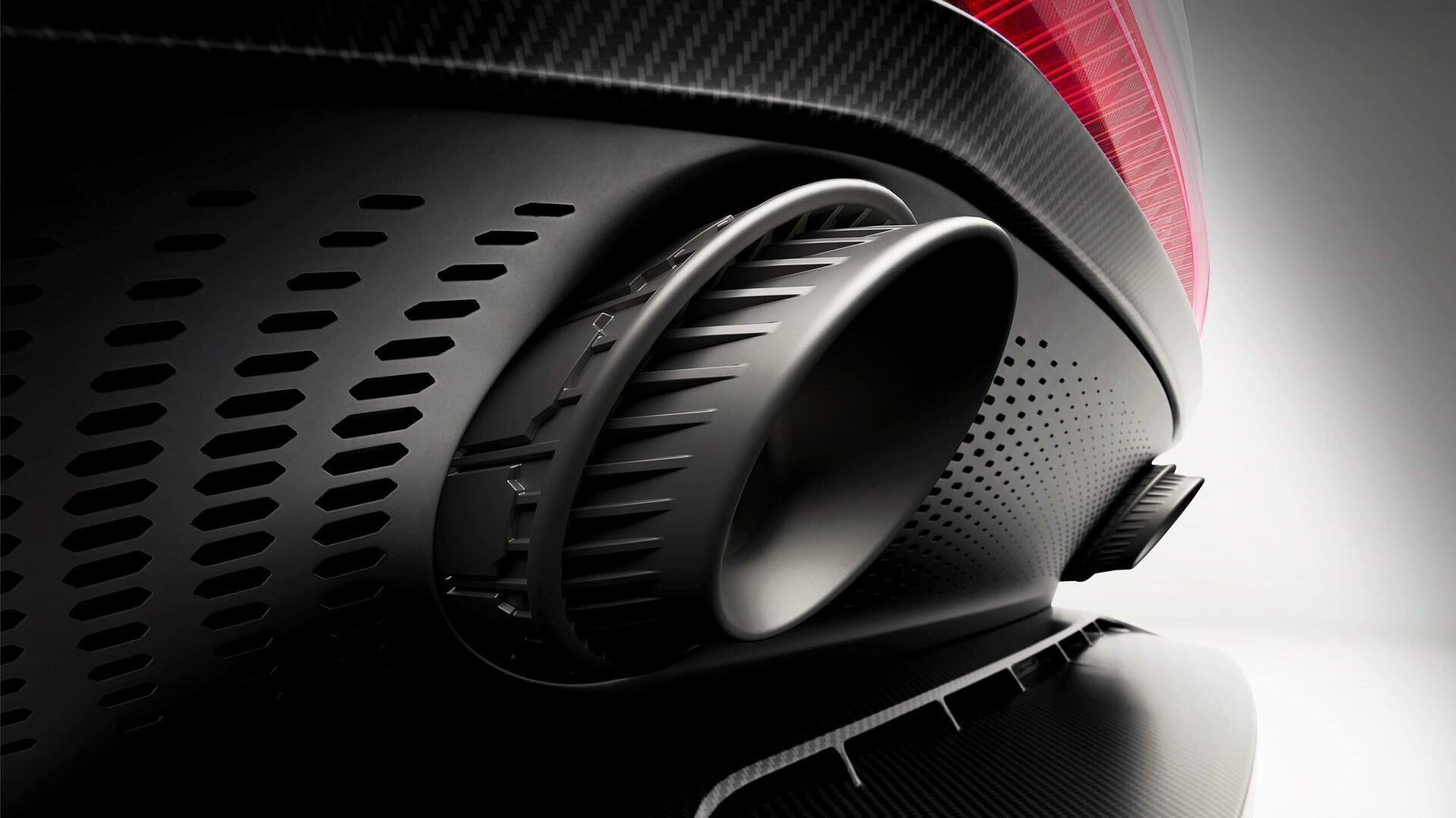 Close-up of a sporty car's exhaust tip on a sleek, carbon-fiber surface with a blurred background.
