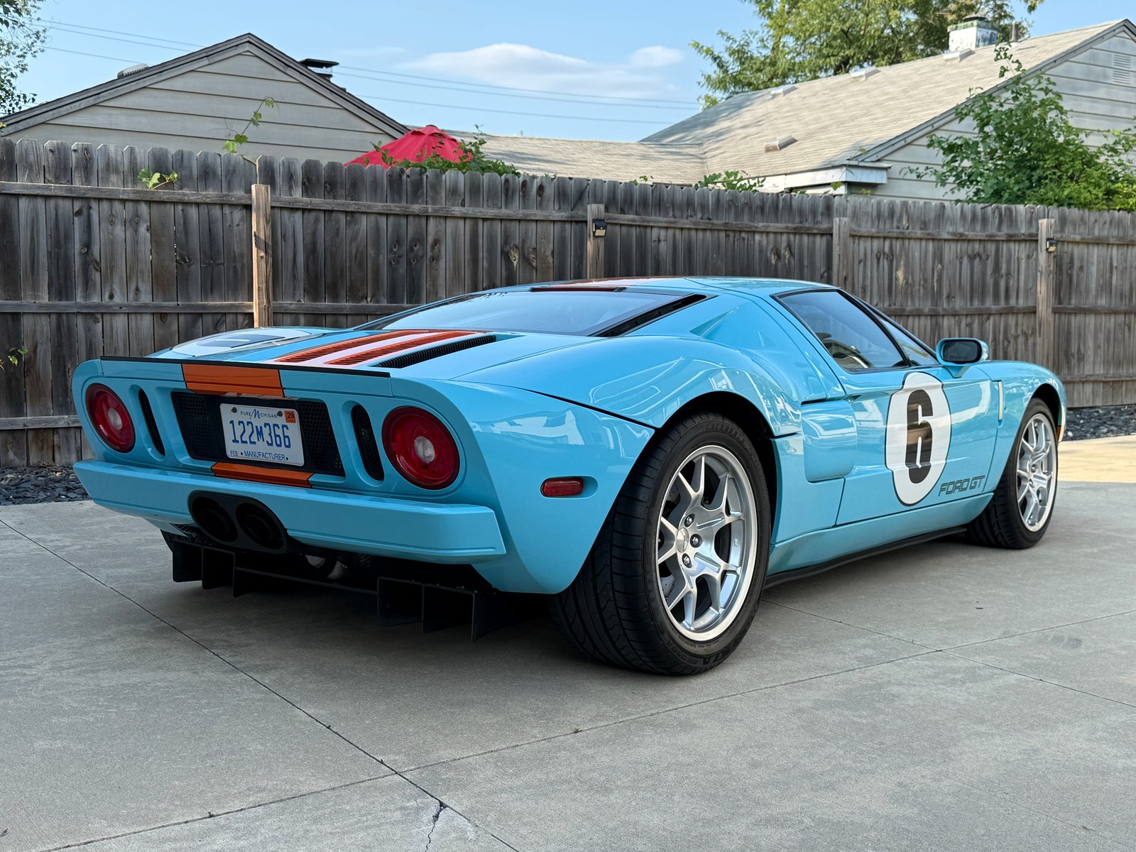 Classic blue Ford GT sports car with racing stripes and number 6, parked on a driveways with wooden fence in the background. Classic blue Ford GT sports car with racing stripes and number 6, parked on a driveways with wooden fence in the background.