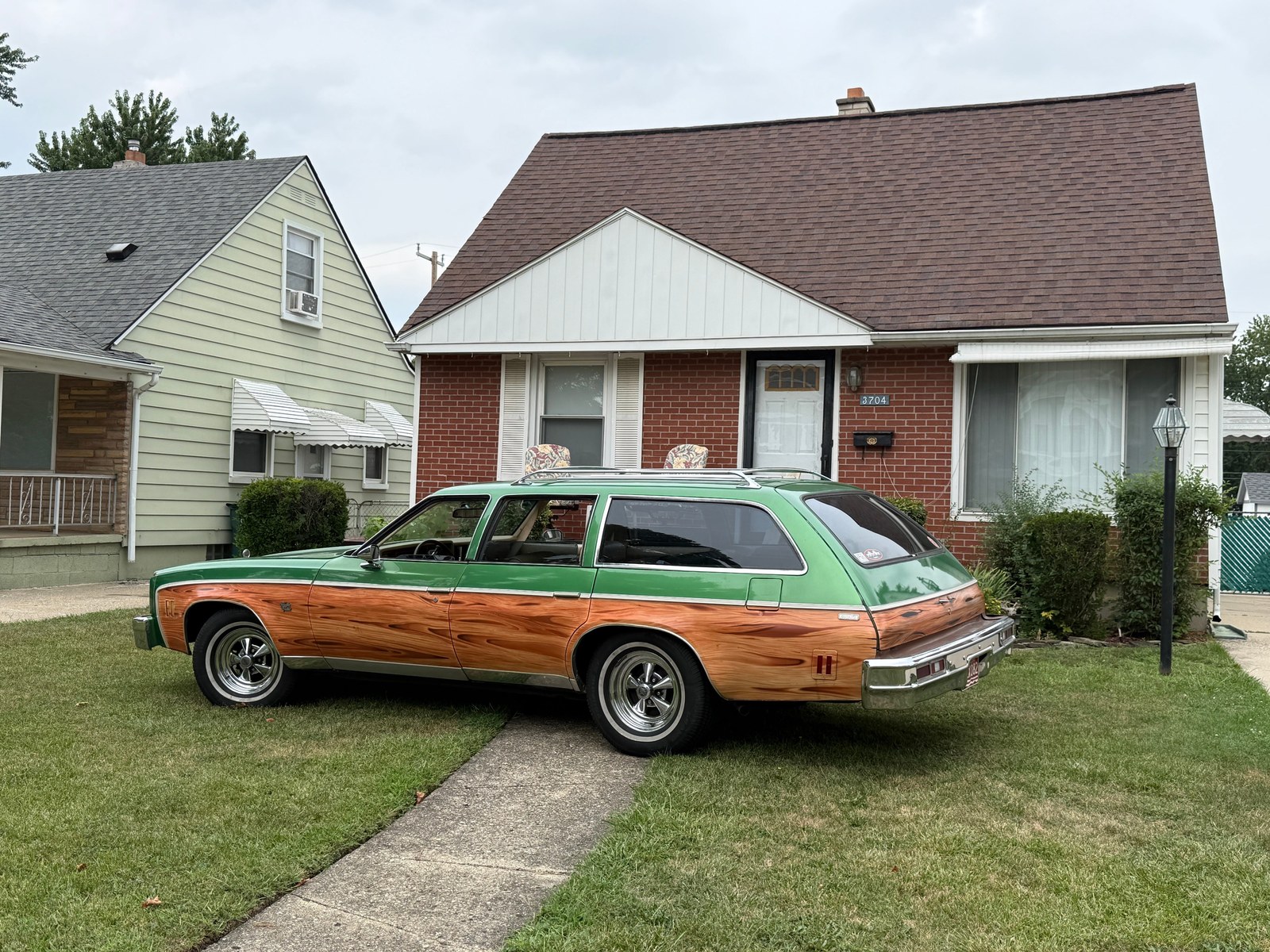 Retro station wagon with wood paneling parked in front of a suburban house on a cloudy day. Retro station wagon with wood paneling parked in front of a suburban house on a cloudy day.