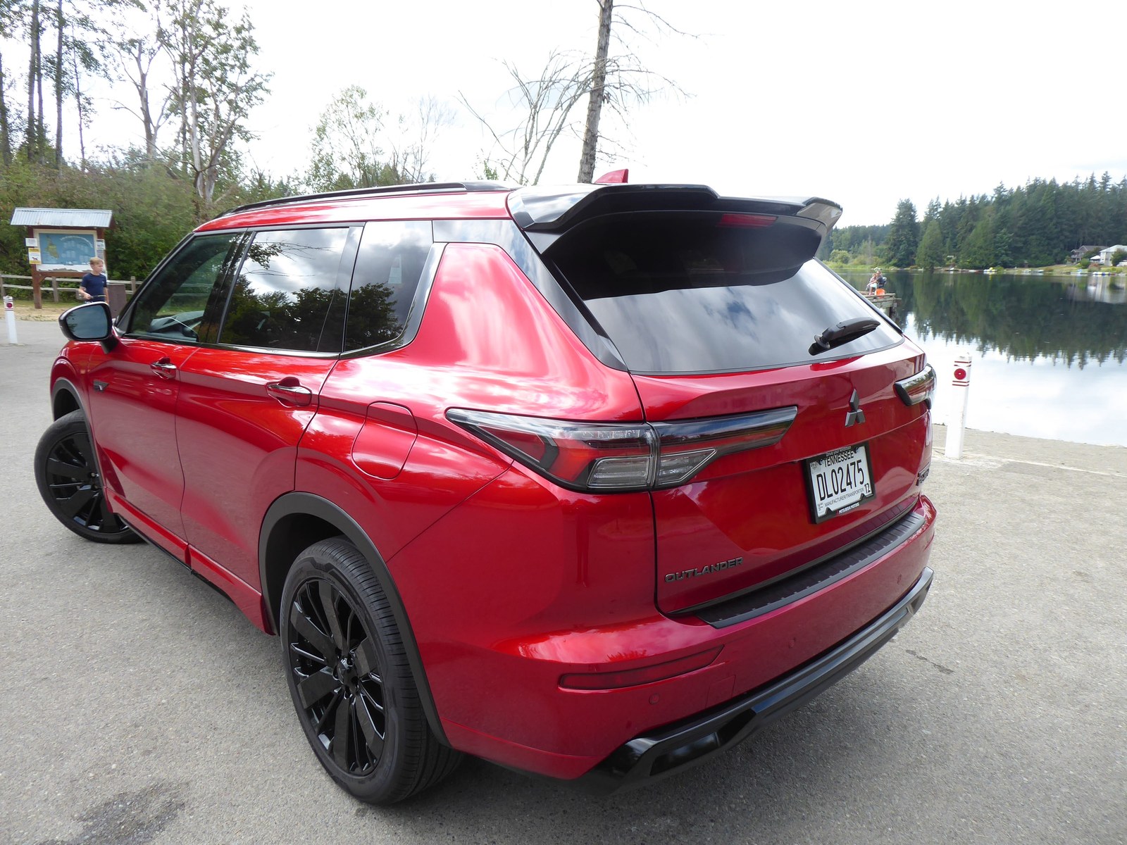 Red Mitsubishi Outlander parked by a lake, showcasing its sleek design and black alloy wheels.