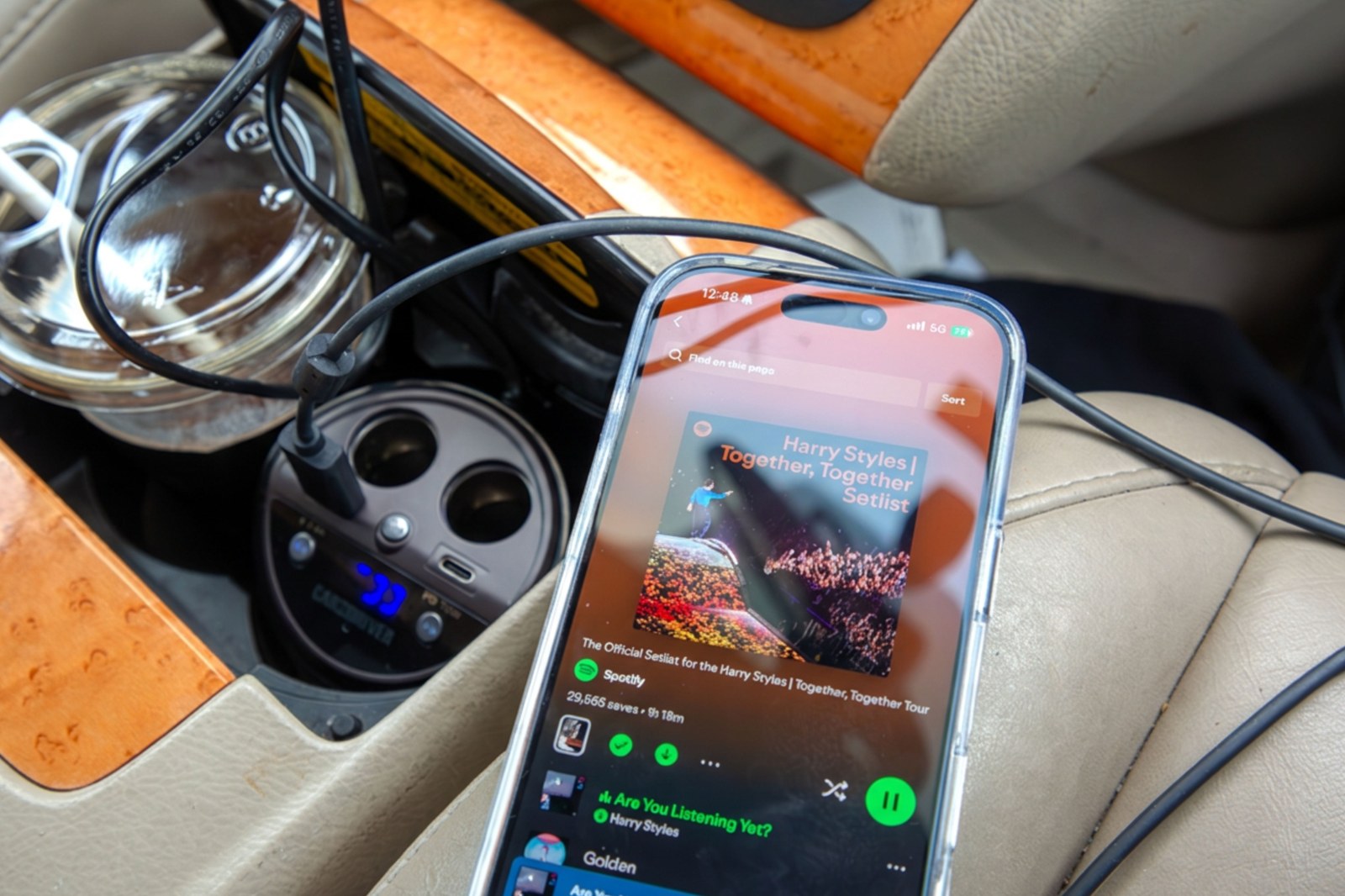 Smartphone displaying Spotify playlist while FM transmitter sits in a car cup holder. Smartphone displaying Spotify playlist while FM transmitter sits in a car cup holder.
