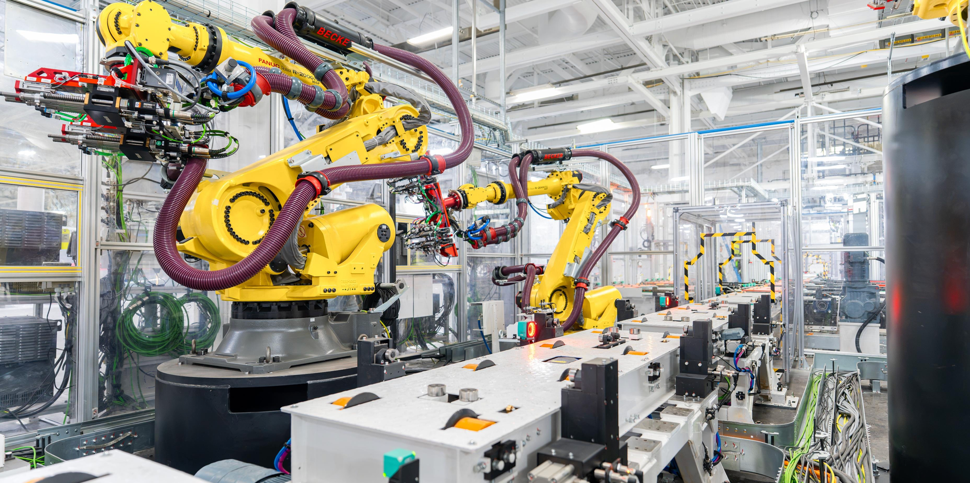 Industrial robotic arms operating in a high-tech manufacturing environment with various components and wiring visible. Industrial robotic arms operating in a high-tech manufacturing environment with various components and wiring visible.