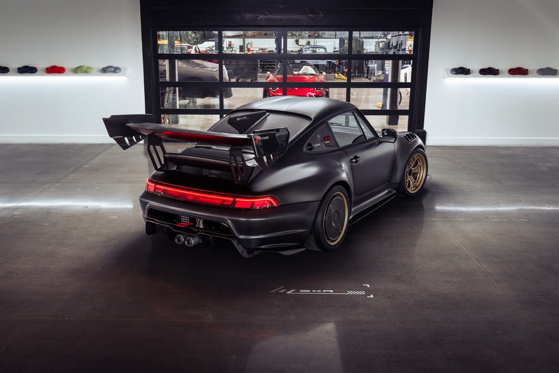 A custom black Porsche 911 with a large rear wing in a modern garage setting.