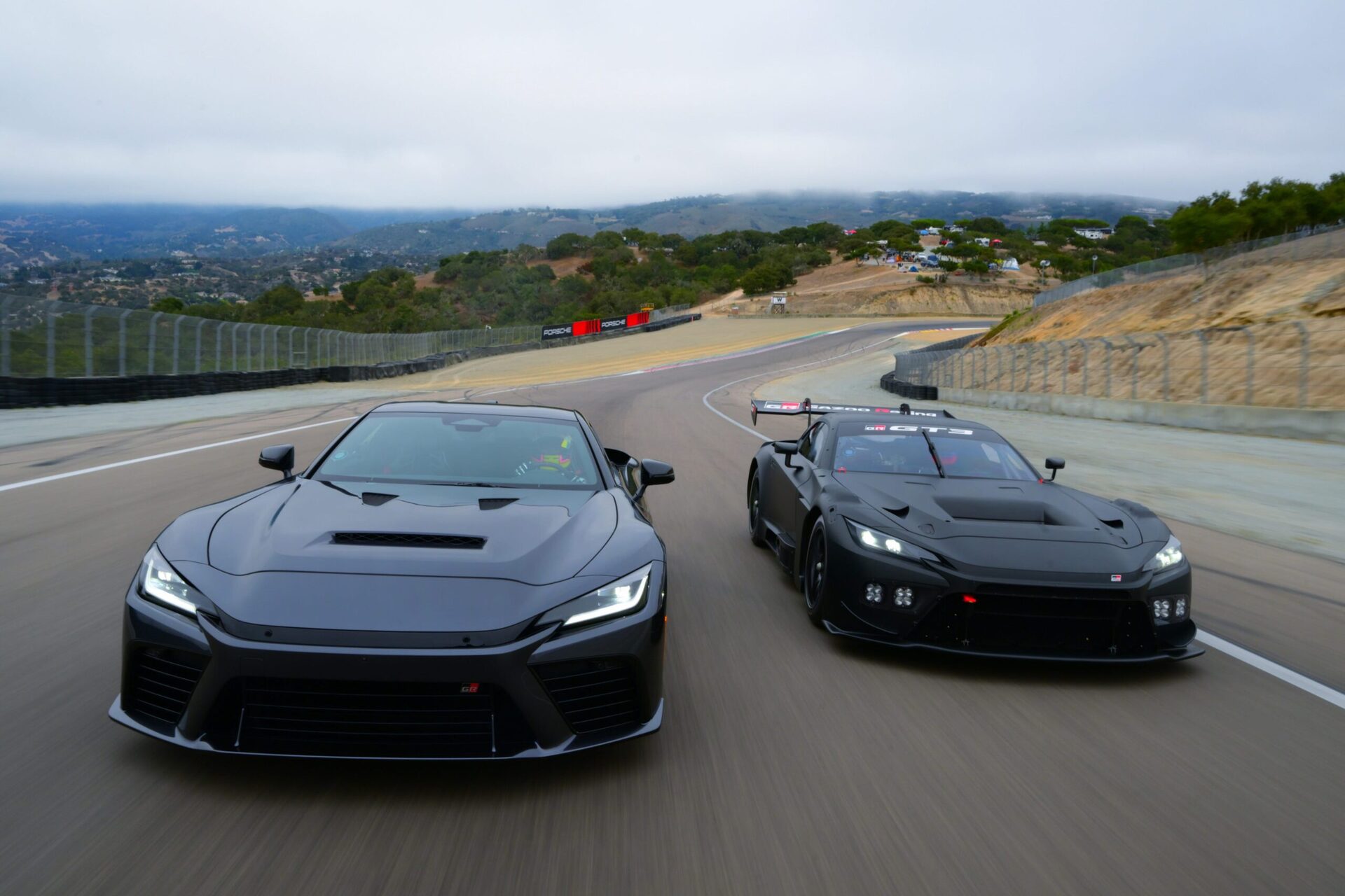 Two sleek black sports cars racing on a winding racetrack surrounded by hills and cloudy skies. Two sleek black sports cars racing on a winding racetrack surrounded by hills and cloudy skies.