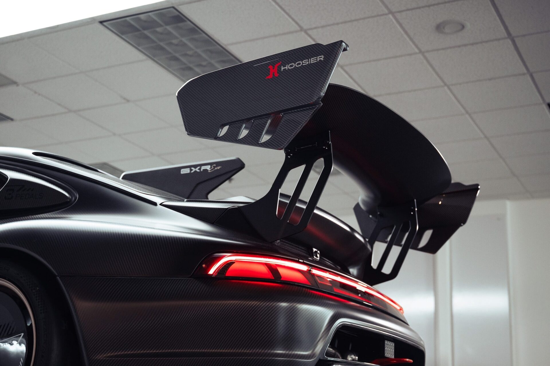 Close-up of a high-performance car's rear featuring carbon fiber wings and a red taillight in a lit interior.