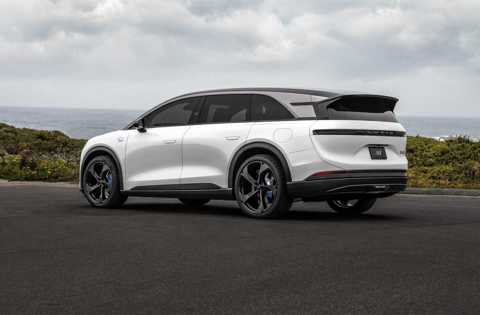 A sleek white electric SUV parked on a road with a coastal view in the background.