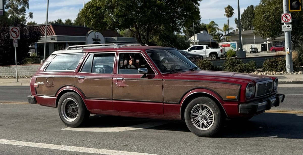 red and wood panel station wagon on city street, driver giving thumbs up.
