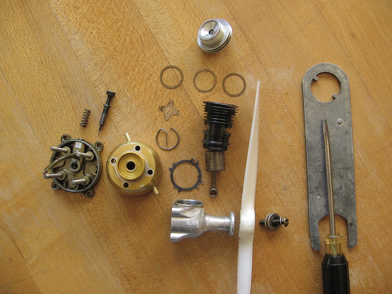 A Cox Babe Bee 0.049 in3 (0.80 cm3) reed valve engine, disassembled, uses glow-plug ignition. Its mass is 64 g.