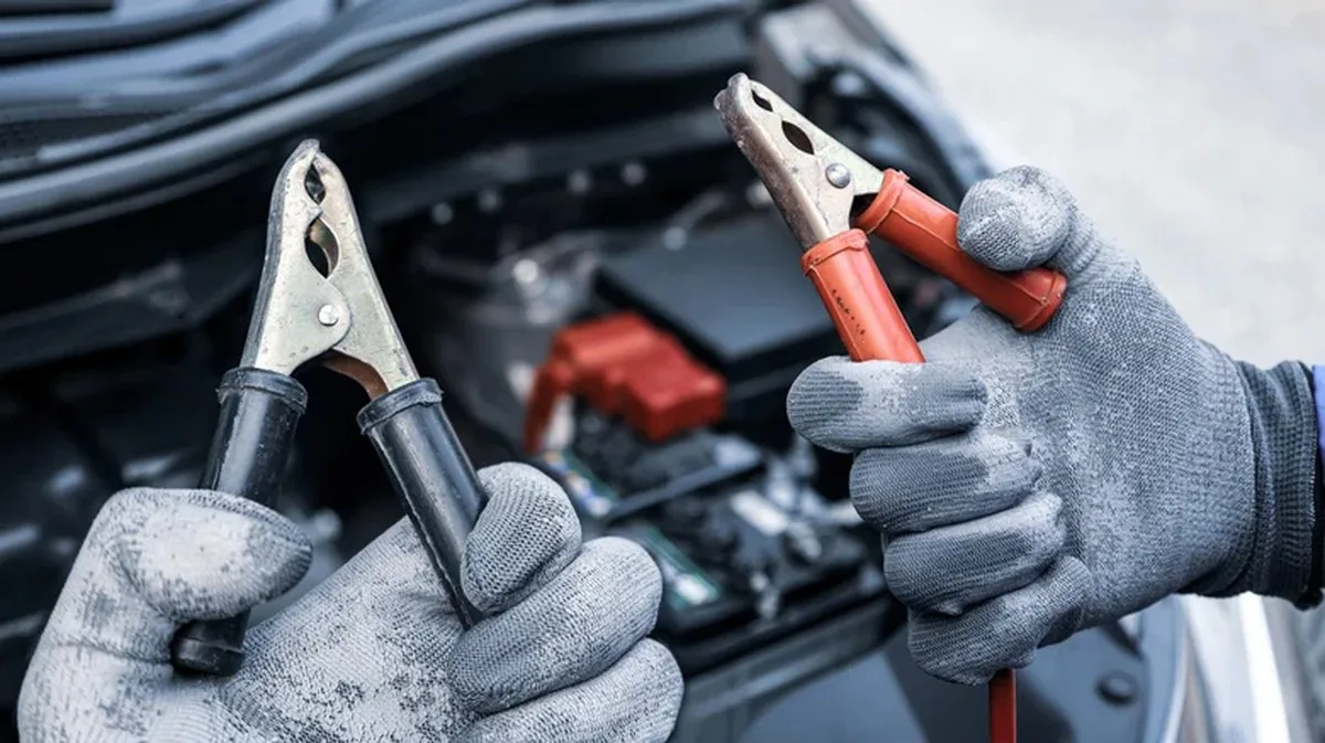 Close up of red and black jumper cables in a mechanic's gloved hands