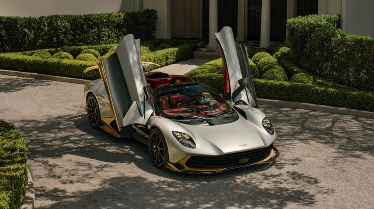 A front three-quarters image of the silver-and-gold Valhalla Spider with its top off and doors up parked in front of a fancy house