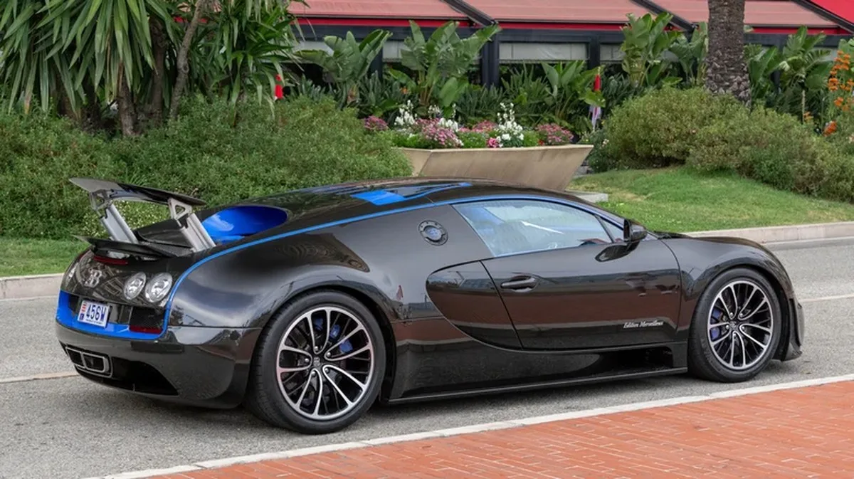 A rear three-quarter view of a dual tone black and blue Bugatti Veyron Super Sport driving through Monaco.