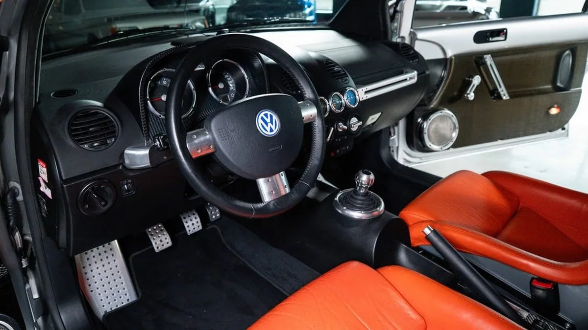 vehicle interior view, black dashboard with sport steering wheel, manual shifter and orange seats.
