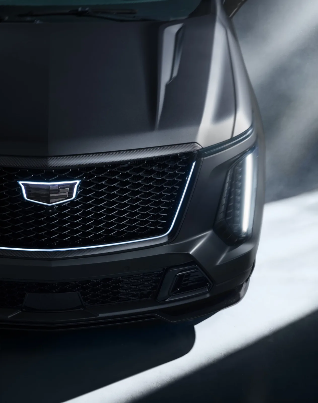 Front view of a matte black Cadillac Escalade-V 125th Anniversary SUV with an illuminated grille emblem and vertical headlights.