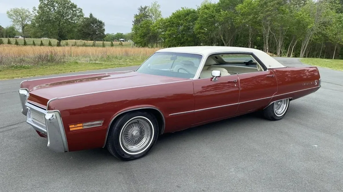 Front three-quarters photo of a burgundy 1973 Chrysler Imperial sedan with a white vinyl roof parked on asphalt in front of grass and trees