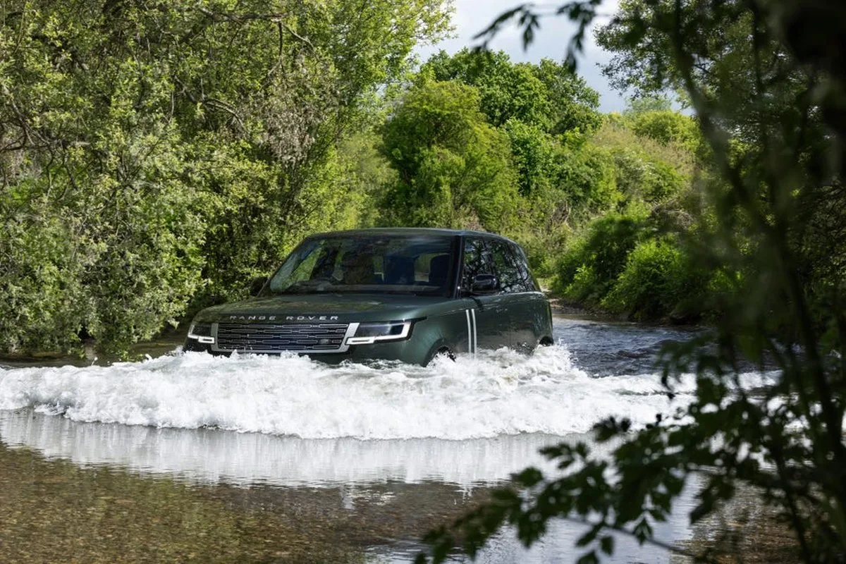 A green Range Rover driving through a shallow stream surrounded by lush greenery. A green Range Rover driving through a shallow stream surrounded by lush greenery.