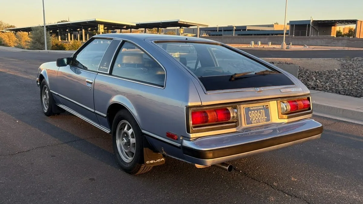 rear three-quarter view, blue vintage coupe parked on paved road with rear hatch and spoiler.