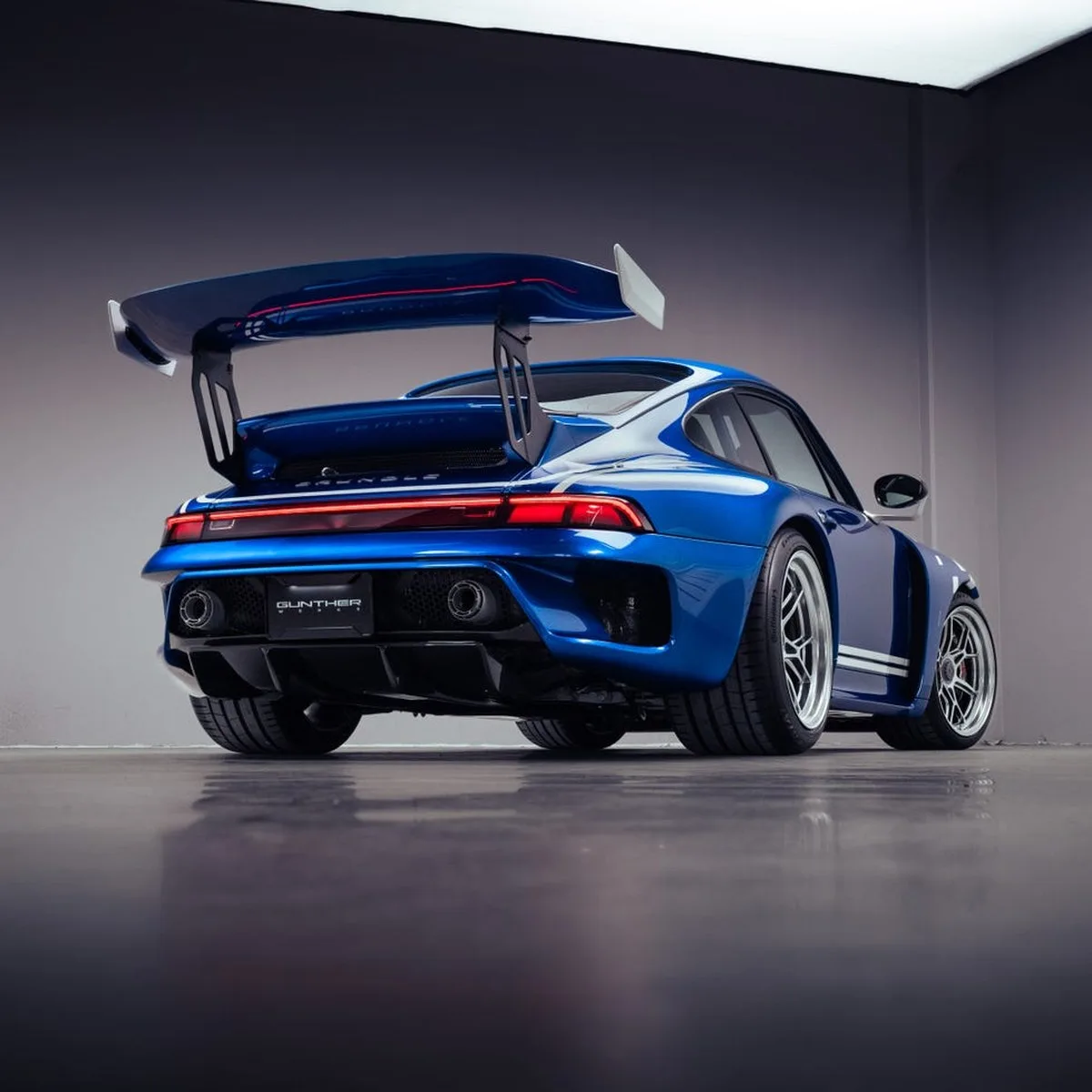 A sleek blue sports car with a large rear wing, showcased in a modern indoor setting. A sleek blue sports car with a large rear wing, showcased in a modern indoor setting.