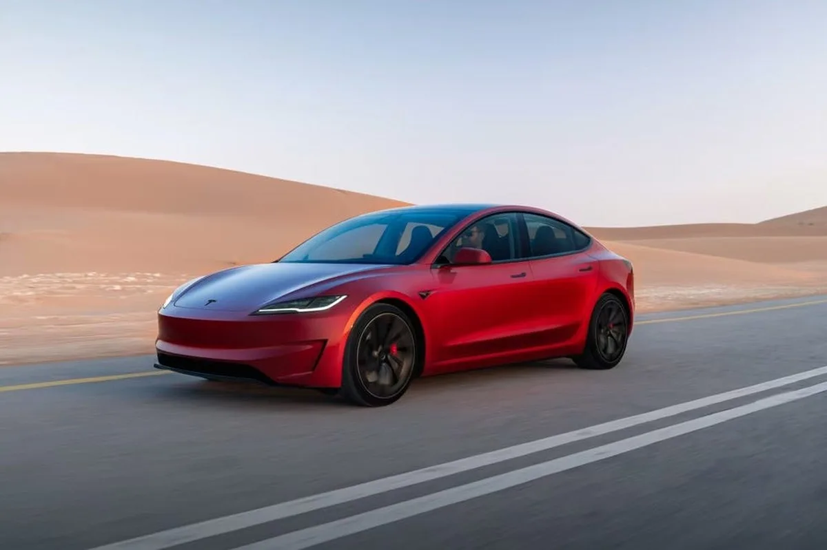 Red electric sedan driving on a deserted road with sand dunes in the background. Red electric sedan driving on a deserted road with sand dunes in the background.