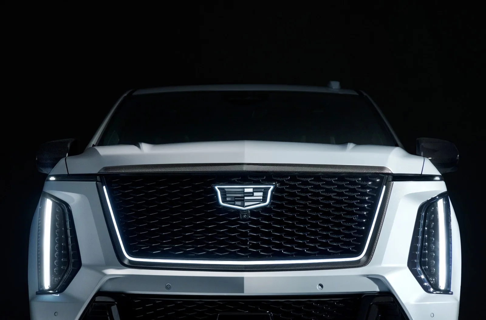 Front view of a white Cadillac Escalade-V 125th Anniversary SUV with an illuminated grille emblem and vertical LED headlights against a black background.
