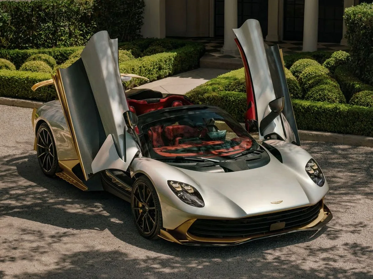 Luxury sports car with vertical doors parked in a well-manicured driveway surrounded by greenery.