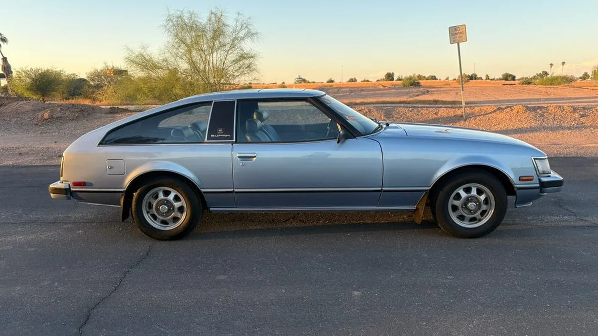 side view, blue vintage coupe parked on paved road with desert landscape.