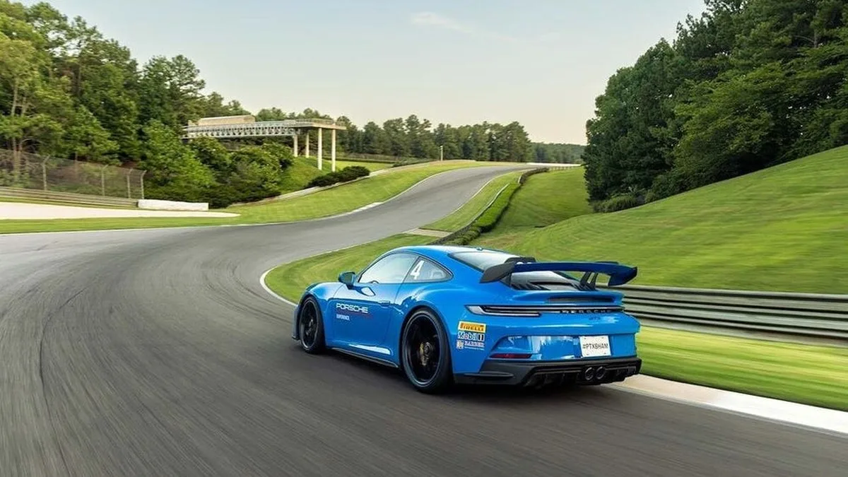 Blue sports car racing on a curved track surrounded by green trees and grass. Blue sports car racing on a curved track surrounded by green trees and grass.