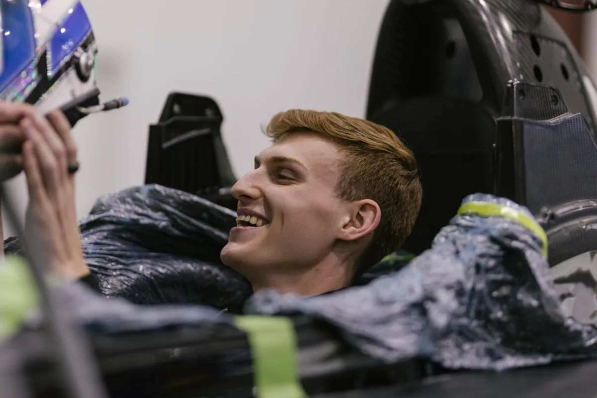 A smiling young man inside a racing simulator, interacting with a helmet and equipment.