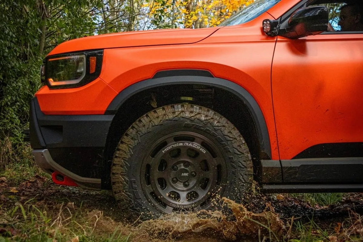 Orange off-road vehicle splashing through water in a forested area with autumn foliage.